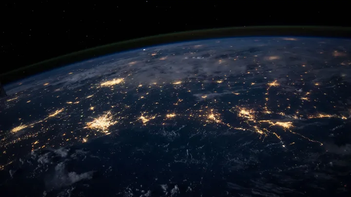 Earth at night seen from orbit, city lights glowing across the dark side of the planet