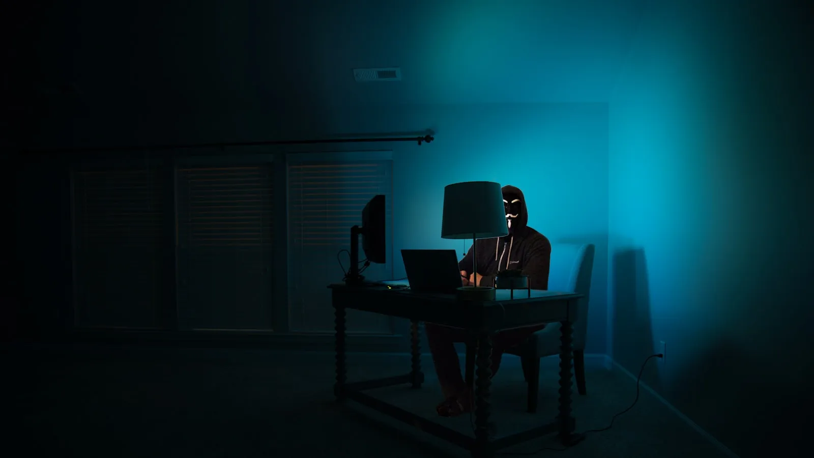A hooded figure at a keyboard in a dark room
