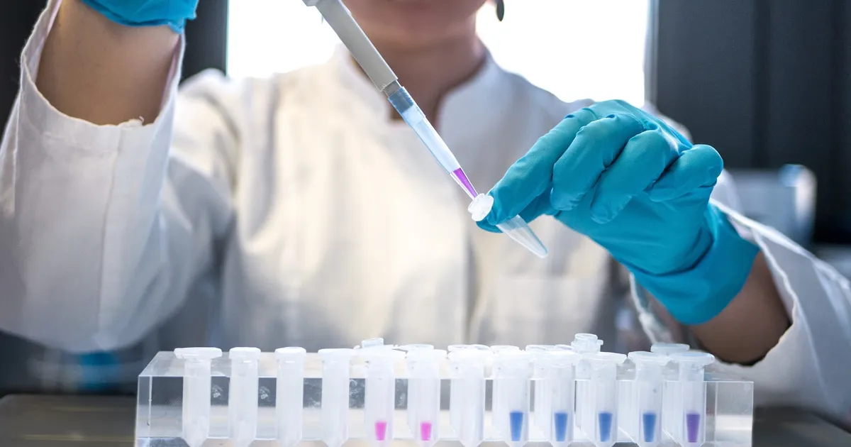 A pipette dispensing liquid into a laboratory tray, representing pharmaceutical research
